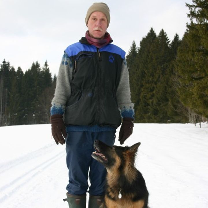 Mann steht im Schnee, ein Schäferhund sitzt vor ihm