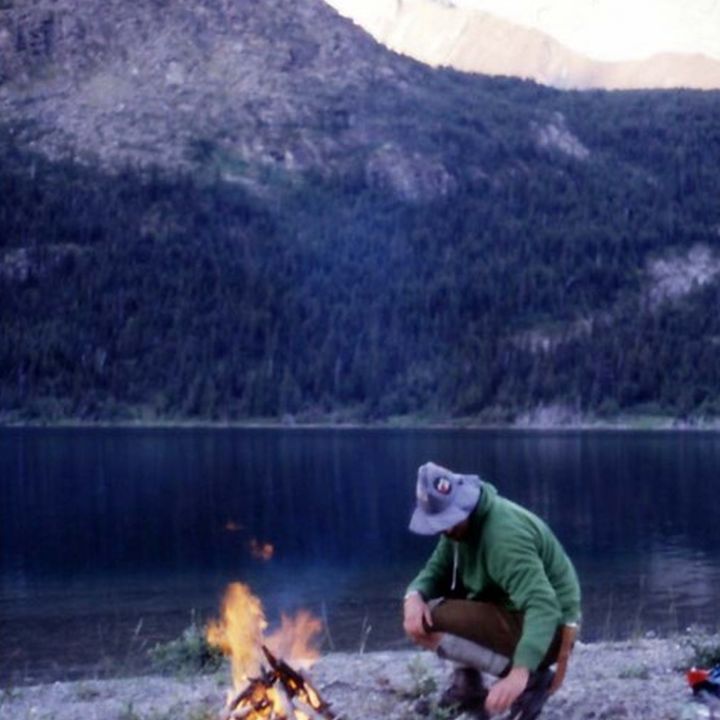 Mann hockt am Lagerfeuer an einem Bergsee
